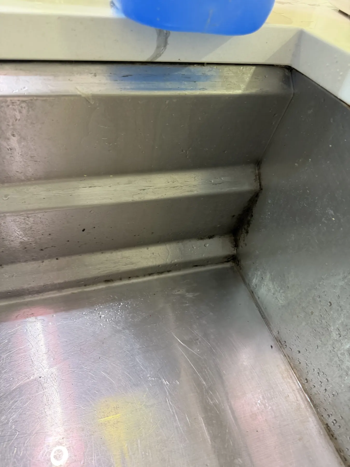 Client-provided before photo showing dark buildup in a stainless-steel sink corner